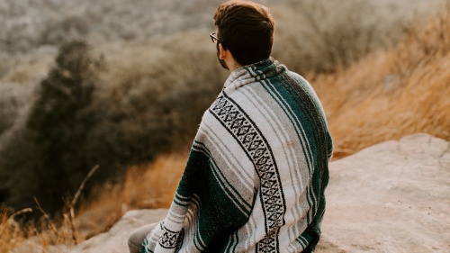 a man wearing a blanket like a robe sitting and looking off over the hilly landscape