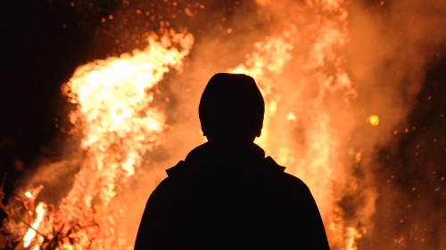the silhouette of a person standing in front of leaping flames of fire