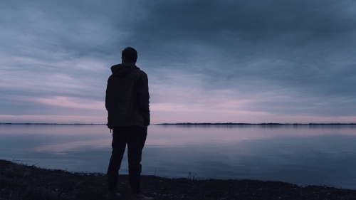A silhouette of a man standing by a lake.